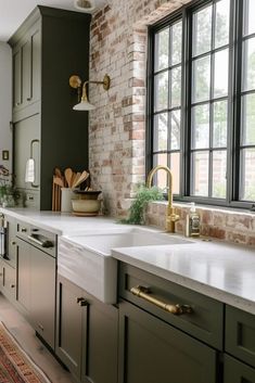 a kitchen with green cabinets and white counter tops next to a brick wall that has black windows