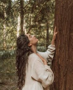 a woman standing next to a tree in the forest