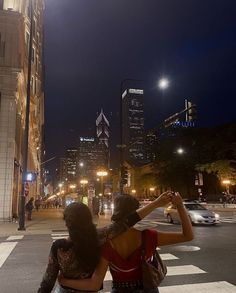 two women are sitting on a crosswalk at night in front of the city skyline