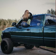 a woman sitting in the bed of a green truck with her long hair sticking out