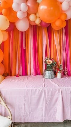 an orange and pink party with balloons, streamers and flowers on the head table