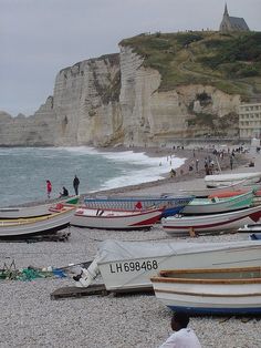 many small boats are on the beach next to the water and people in the background