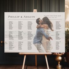 a wedding seating chart on a easel in front of a black wall and potted plant