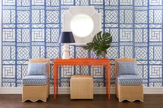 two chairs and a table with a mirror on it in front of a blue patterned wall