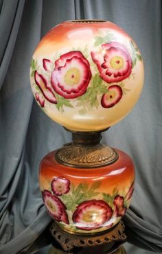 a vase with flowers painted on it sitting on top of a wooden stand in front of a curtain