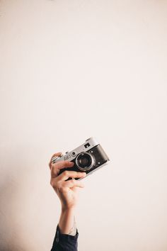 a person holding up a camera in front of a white wall