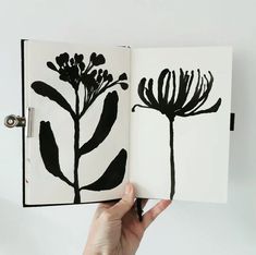 a hand holding an open book with black flowers on it