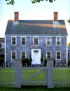 a large gray house with a white picket fence and an american flag on the front door