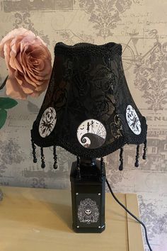 a table lamp with a black shade on it and a pink flower in the corner