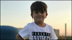 a young boy standing in front of a blue water tank with the sun setting behind him