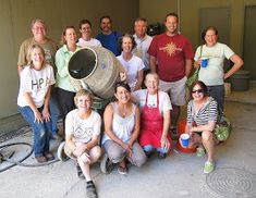 a group of people standing and sitting in front of a building with an airplane propellor