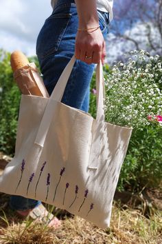 a person carrying a bag with lavender flowers on it in the grass and bushes behind them