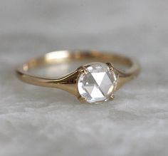 a gold ring with a white diamond in the center on top of a marble surface