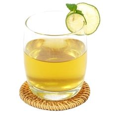 a glass filled with liquid next to a slice of lime and a wicker coaster