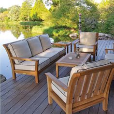 a wooden deck with chairs and tables next to a river in the background, surrounded by greenery