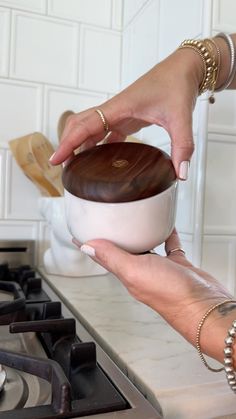 a woman is holding a bowl in her hand while standing next to a stove top