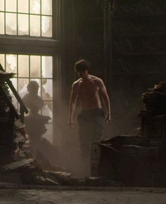 a shirtless man standing in front of a window next to a pile of junk