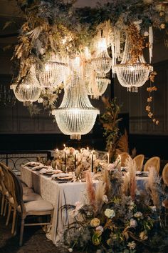 a dining room table with chandelier and flowers on the table, surrounded by greenery