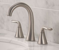 two faucets on a marble countertop in a white tiled bathroom with grey and gray tiles