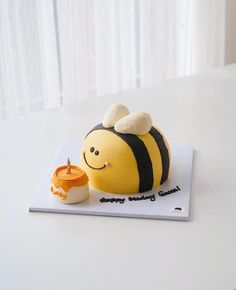 a cake shaped like a bee sitting on top of a white table next to a cup