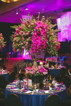 a tall vase filled with pink flowers sitting on top of a blue table cloth covered dining room