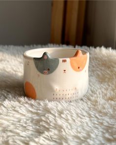 a white cat bowl with orange and gray cats on it sitting on a fluffy rug