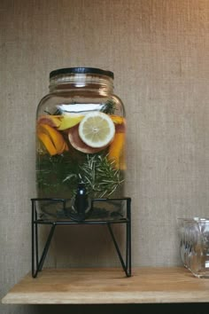 a glass jar filled with water and lemon slices on top of a wooden shelf next to two glasses