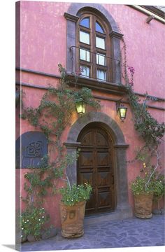 a pink building with potted plants in front of it and an arched window above the door