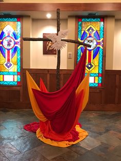 a cross with stained glass windows in the background and a colorful cloth draped around it