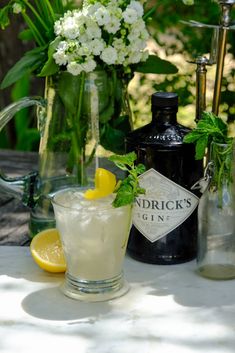 a table topped with bottles and glasses filled with liquid next to lemons, mint leaves and flowers