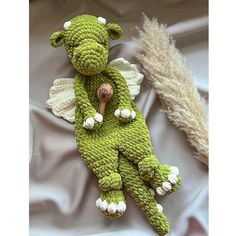 a crocheted green teddy bear laying on top of a bed next to a feather