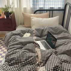 a laptop computer sitting on top of a black and white checkered comforter in a bedroom