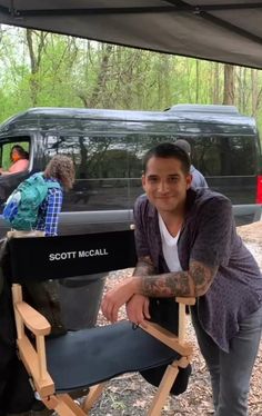 a man sitting in a folding chair next to a van with people standing around it