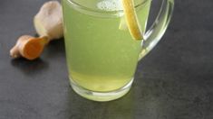 a pitcher filled with green liquid next to an orange peel and ginger on a table