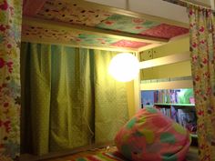 a bedroom with yellow walls and colorful curtains on the window sill, next to a book shelf