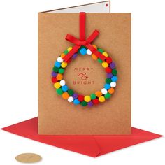 a card with a christmas wreath and pom - poms on it, next to a penny