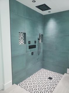 a bathroom with green walls and black accents on the shower head, tile floor, and rug