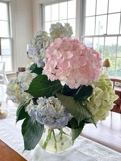 a vase filled with pink and blue flowers on top of a table next to two windows