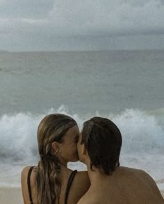 a man and woman kissing on the beach with waves in the backgroung