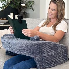 a woman sitting on a couch holding a book and smiling at the camera while looking at it