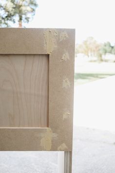 a wooden frame with paint on it sitting in front of a tree and grass area