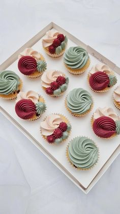 twelve cupcakes in different colors on a white tray with red and green frosting