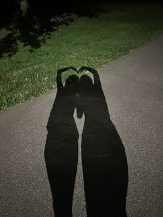 the shadow of two people's hands making a heart shape in the middle of the road