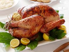 a roasted turkey on a platter with lemons and leaves in the foreground