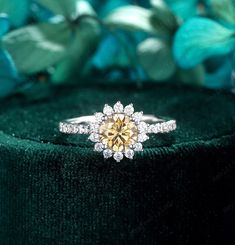 a yellow diamond ring sitting on top of a green velvet covered box with flowers in the background