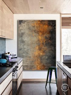 an abstract painting hangs on the wall in a kitchen with wooden cabinets and stools