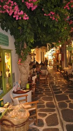 an alley way with tables and chairs lined up along the wall, covered in pink flowers