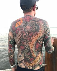 a man with tattoos on his back looking out at the ocean from a boat deck