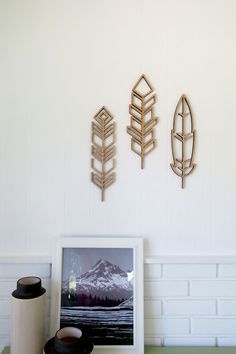 three metal arrows are mounted on the wall above a table with a cup and vase