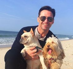 a man sitting on the beach with two dogs